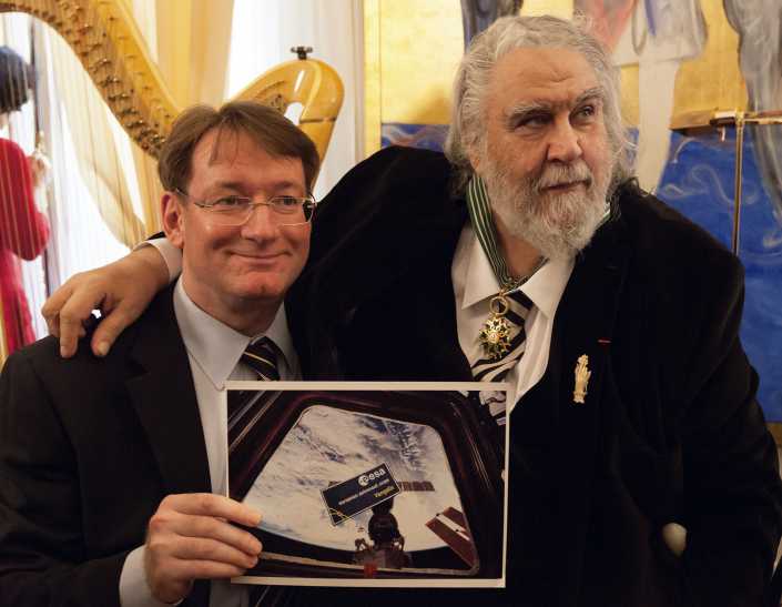 Carl Walker shows Vangelis a photograph of his badge, floating inside the International Space Station
